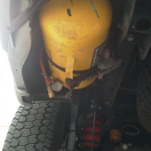 5 gallon air tank mounted up under rear left corner of bed.   A bracket welded to the top secures it to one of the bed's frame rails, and the strap is